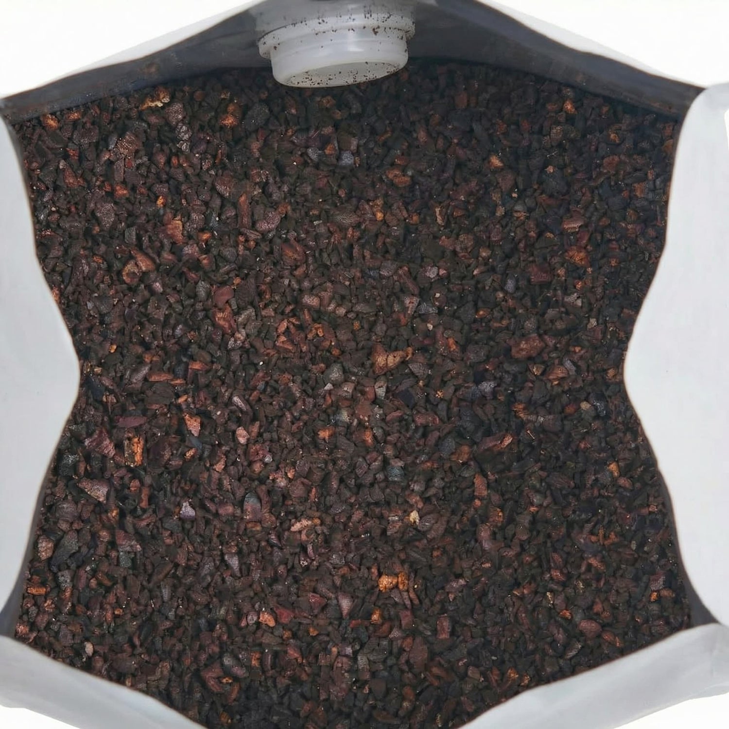 Close-up of dark brown coarse ground coffee beans for cold brew in a container with a light source above.