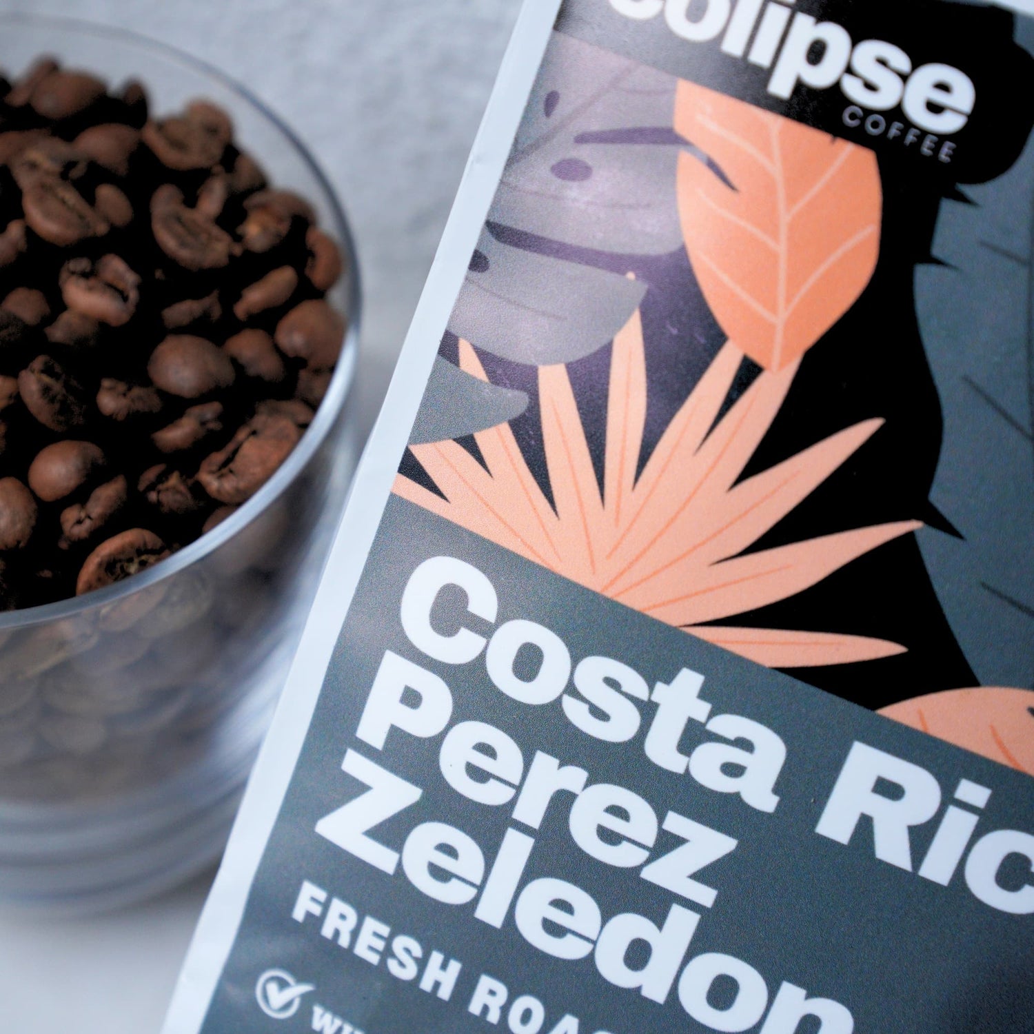 Cup of coffee beans next to a package of Colipse Coffee Costa Perez Zeledon