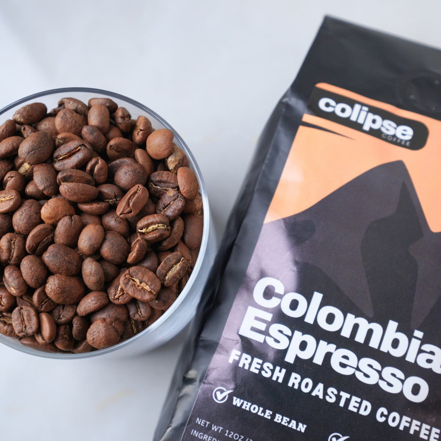 Colombia Espresso coffee beans in a bowl with a Colipse Coffee package on a white background