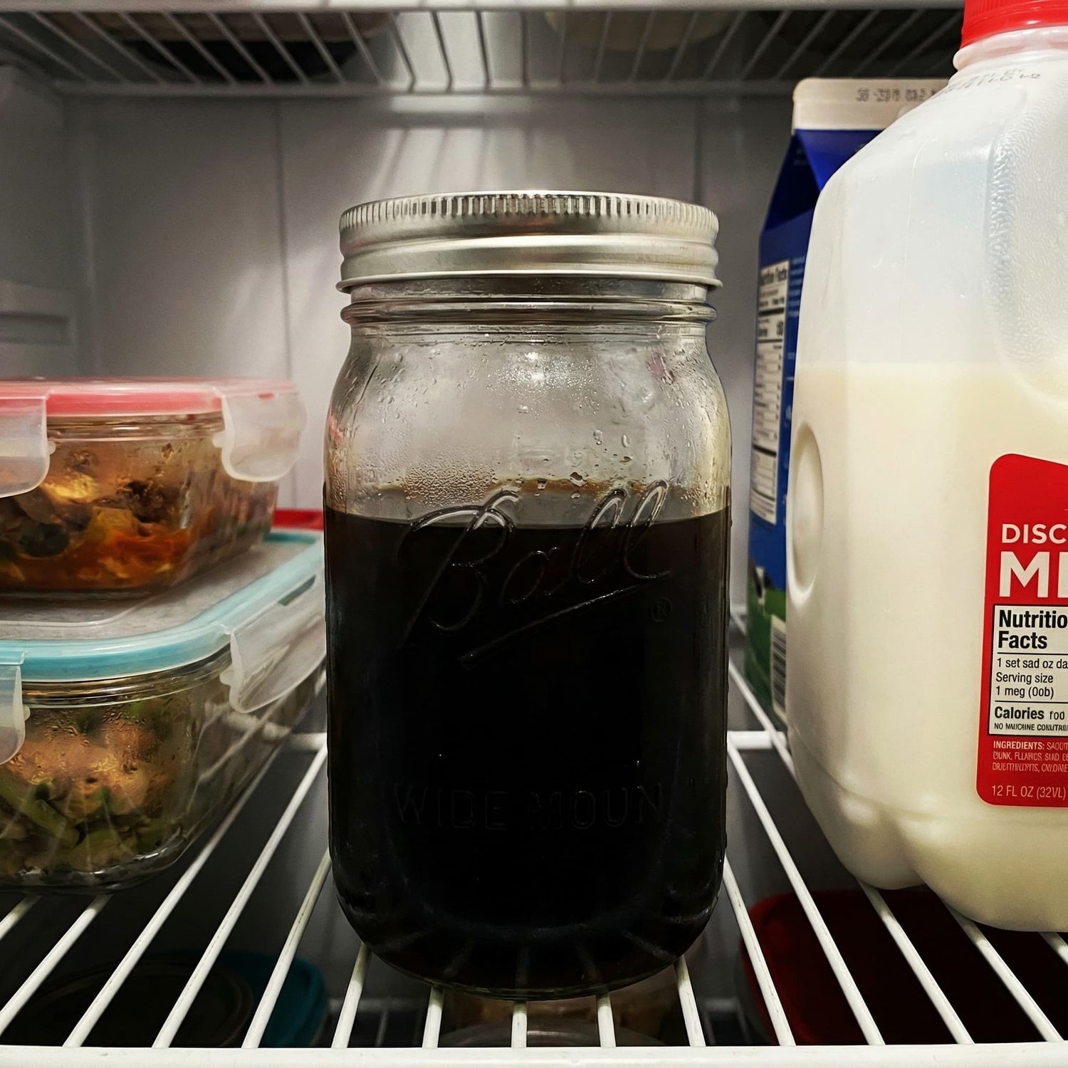 Mason jar with dark cold brew coffee on a refrigerator shelf with milk and other items.
