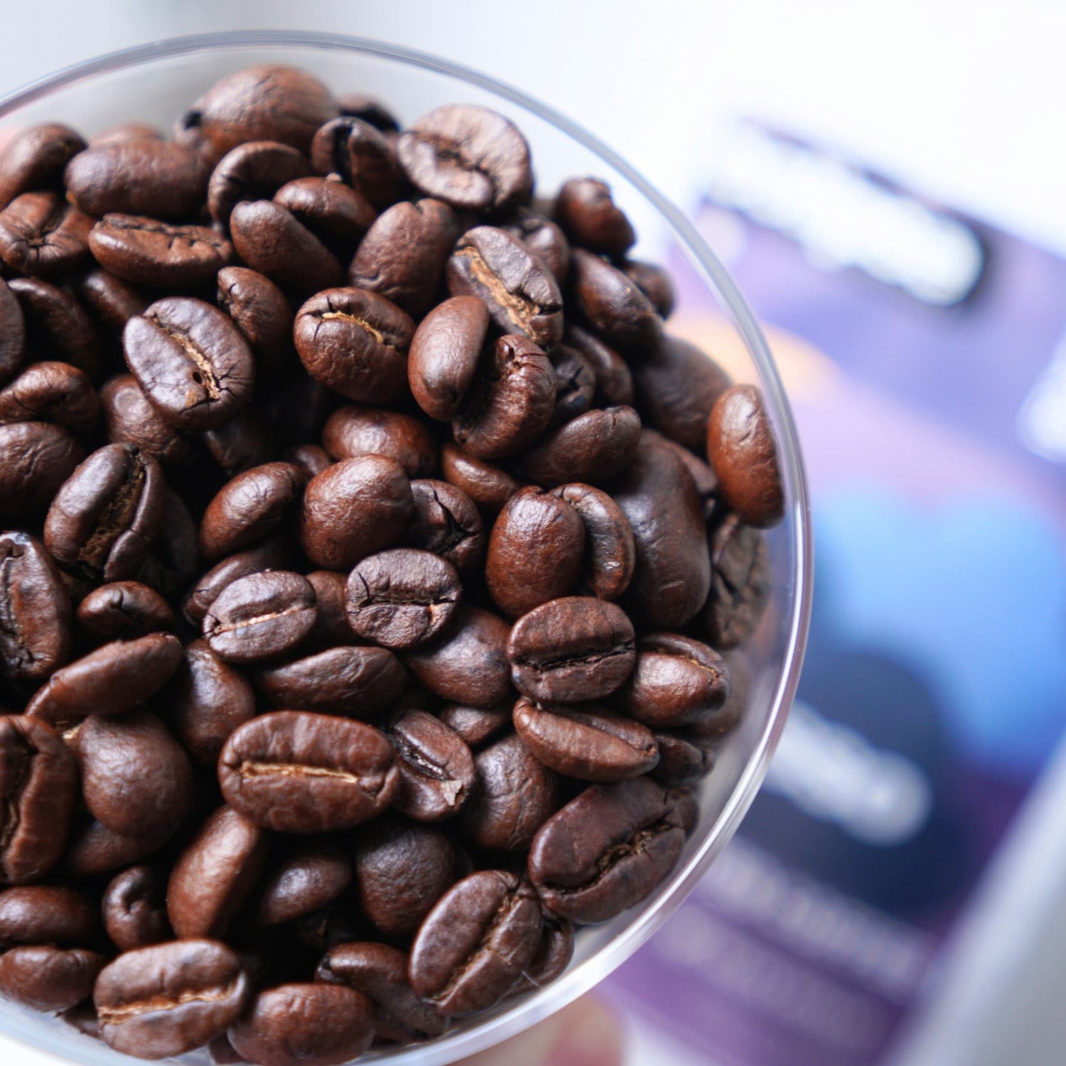 Close-up of roasted espresso coffee beans in a transparent container with a blurred background