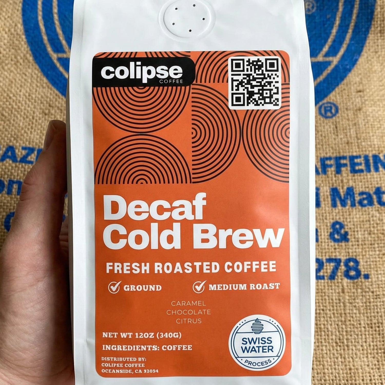 Colipse Decaf Cold Brew coffee package held in front of a burlap background with visible branding.