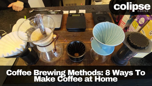 This image shows a variety of coffee brewing equipment laid out on a wooden table, including a kettle, grinder, scale, and several different brewing devices