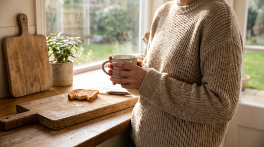 Person holding a warm mug of mushroom coffee at a bright kitchen counter in the morning