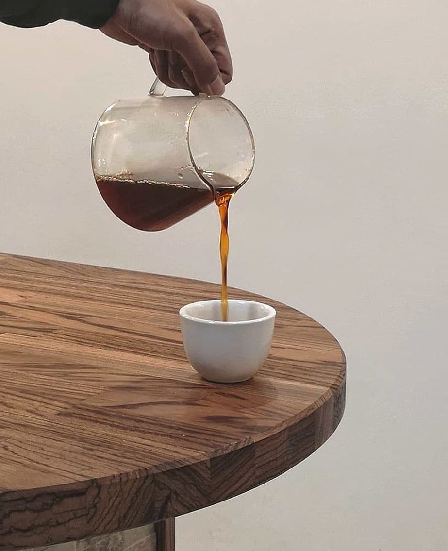 Pouring coffee half caffeine from a glass carafe into a small cup.