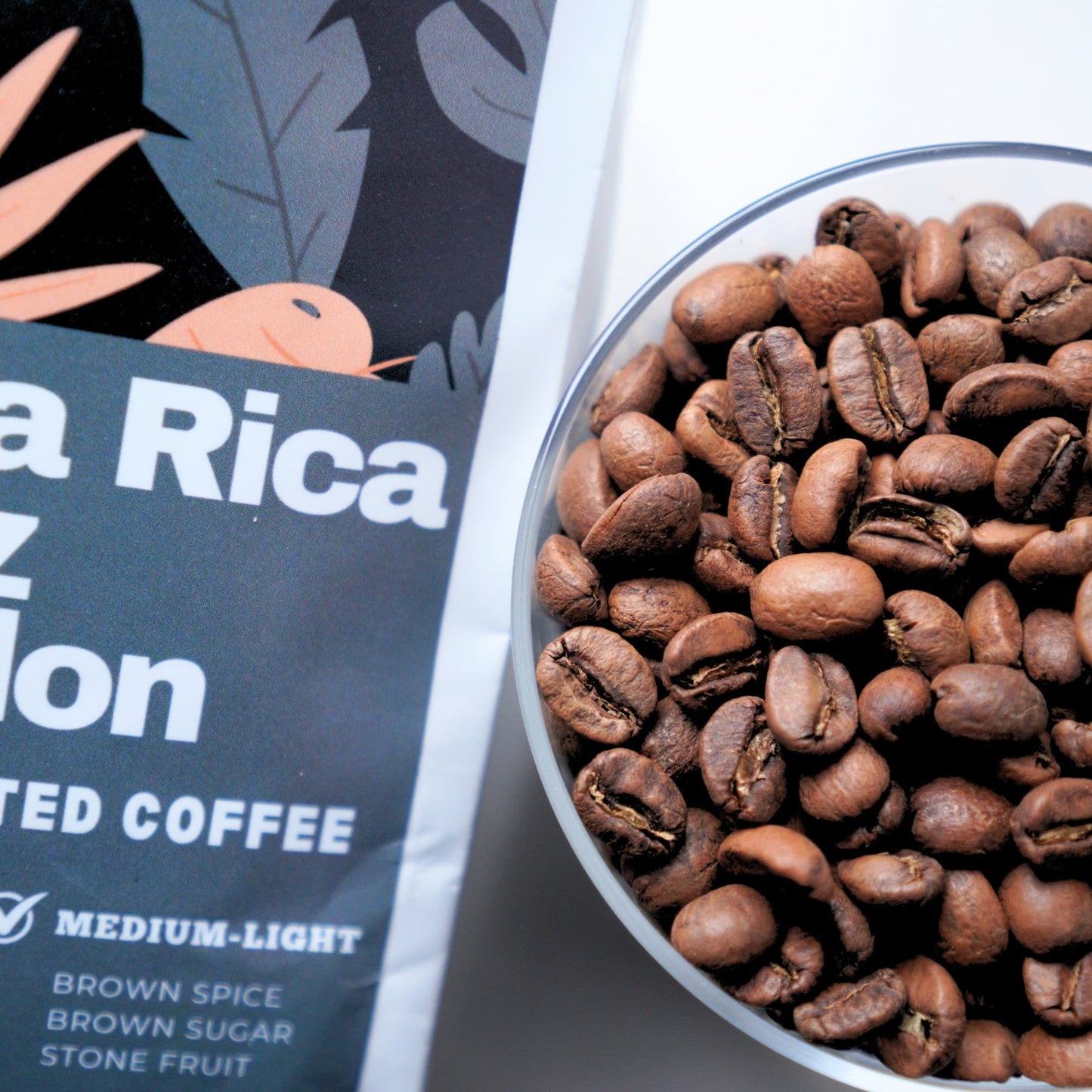 Coffee beans in a bowl with a coffee package labeled 'Costa Rica' on a white background