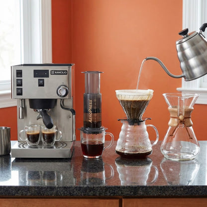 Coffee-making setup with espresso machine, Aeropress, and pour-over coffee on a countertop.