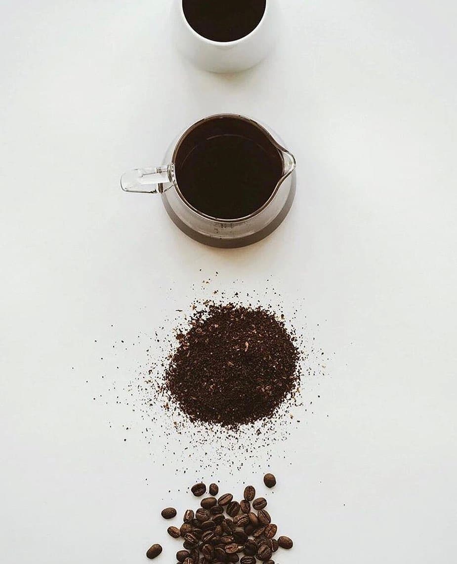 Flat lay of coffee elements: beans, grounds, carafe with half-decaf coffee, and a cup.