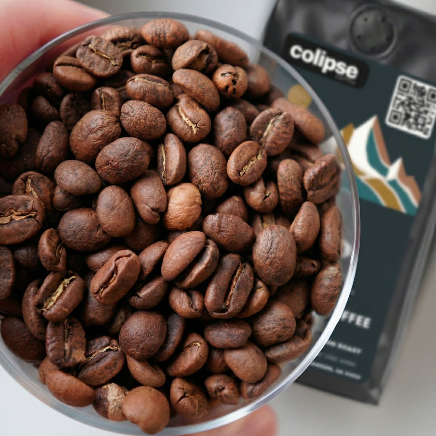 Close-up of coffee beans in a container with Colipse coffee packaging in the background.