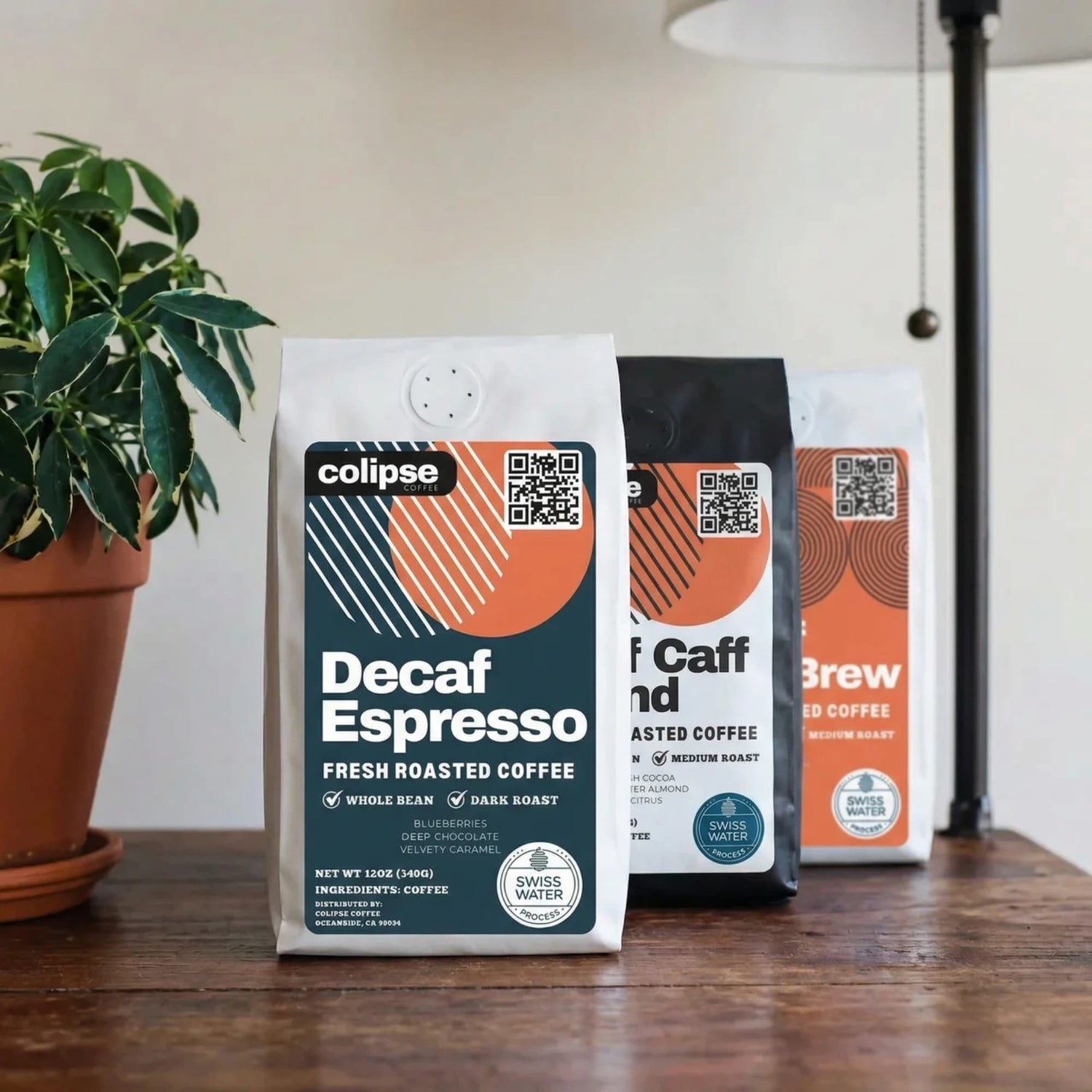 Three coffee bags from colipse on a wooden surface with a plant in the background